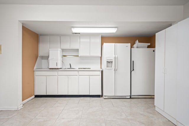 kitchen with light countertops, freestanding refrigerator, white fridge with ice dispenser, white cabinets, and a sink