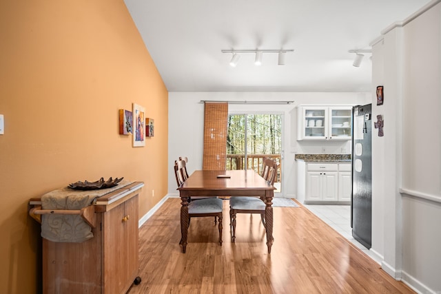 dining room featuring track lighting, light wood-style flooring, and baseboards
