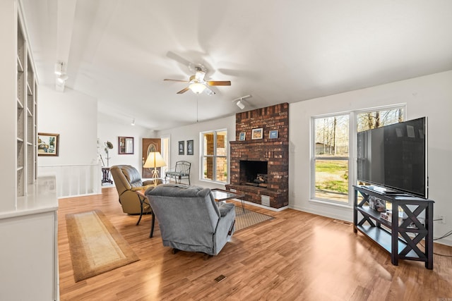 living area featuring vaulted ceiling, a fireplace, light wood finished floors, and ceiling fan