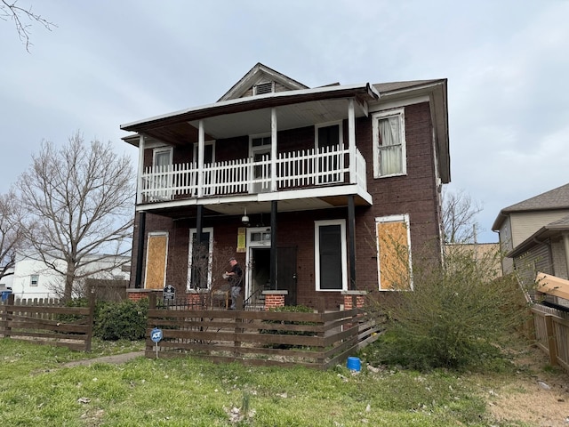 view of front of house featuring a balcony, brick siding, and a fenced front yard