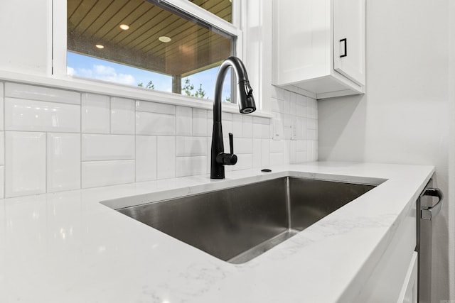 kitchen view of a sink, white cabinetry, tasteful backsplash, light stone counters, and recessed lighting