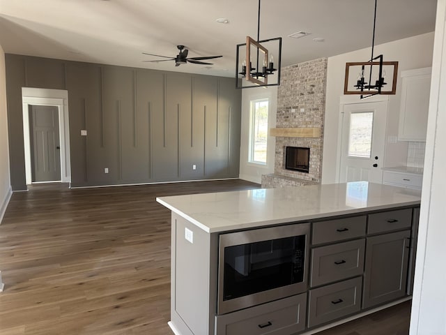 kitchen featuring wood finished floors, stainless steel microwave, ceiling fan with notable chandelier, open floor plan, and a wealth of natural light