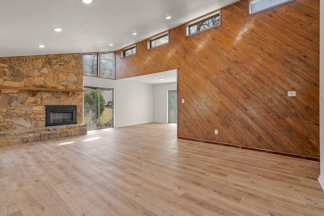 unfurnished living room featuring plenty of natural light, a stone fireplace, light wood-style flooring, and wood walls