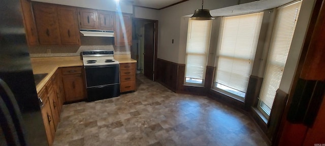 kitchen featuring black refrigerator, a wainscoted wall, light countertops, range with electric stovetop, and exhaust hood