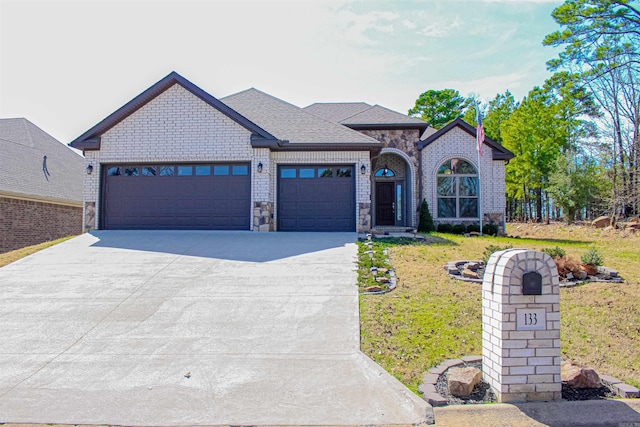 view of front of home with a front lawn, driveway, stone siding, roof with shingles, and a garage