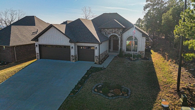 french country inspired facade featuring a front lawn, roof with shingles, driveway, stone siding, and an attached garage