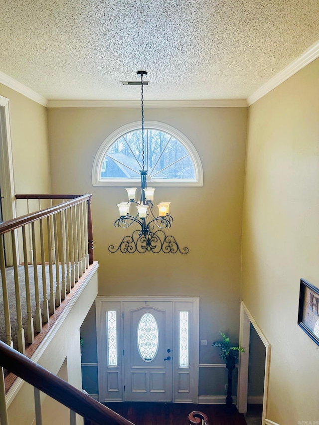 entrance foyer with visible vents, ornamental molding, a textured ceiling, a towering ceiling, and a chandelier