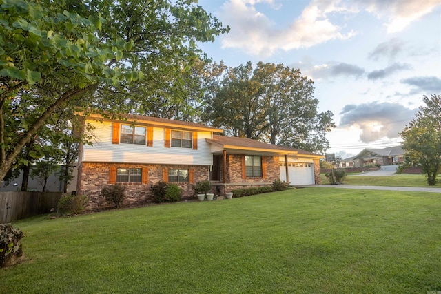 split level home with fence, a front yard, a garage, stone siding, and driveway