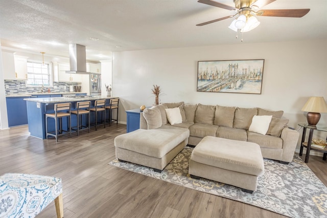 living area with light wood-style flooring, a ceiling fan, baseboards, and a textured ceiling