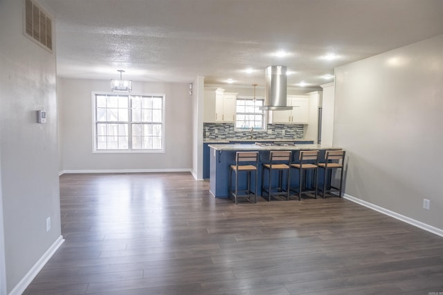 kitchen featuring visible vents, backsplash, a kitchen breakfast bar, island exhaust hood, and white cabinetry