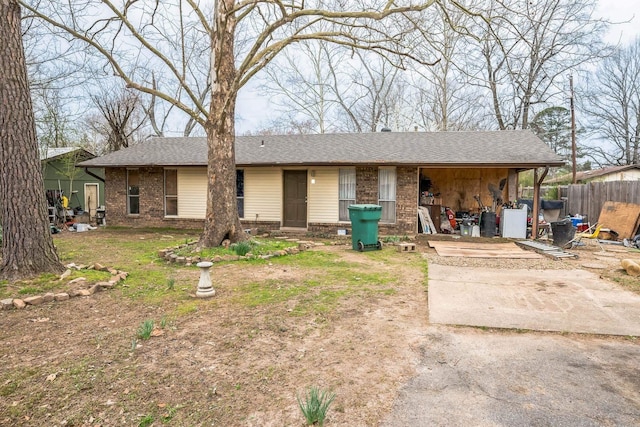 view of front of house featuring brick siding, a shingled roof, a carport, and fence