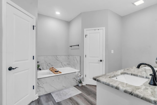 full bath featuring vanity, a garden tub, and wood finished floors