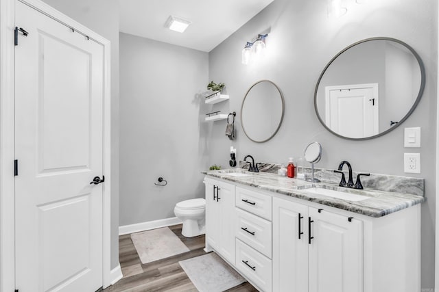 bathroom with double vanity, toilet, wood finished floors, and a sink