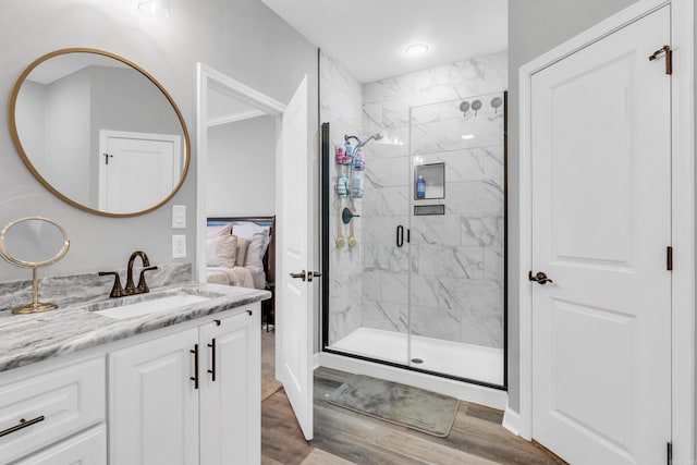 bathroom featuring vanity, wood finished floors, a marble finish shower, and connected bathroom