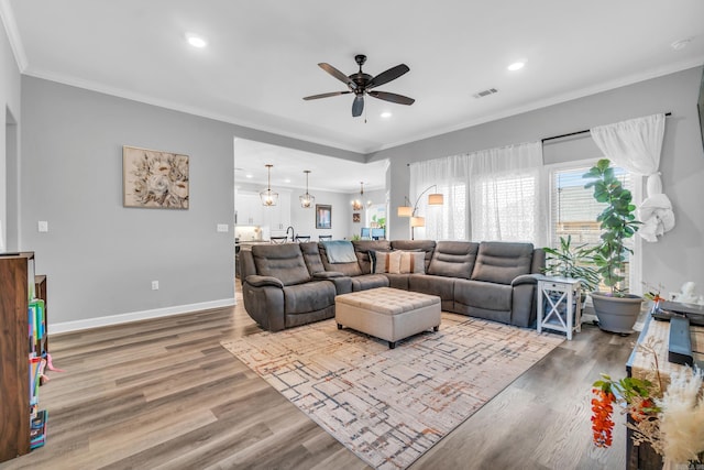 living room with wood finished floors, baseboards, a ceiling fan, visible vents, and ornamental molding