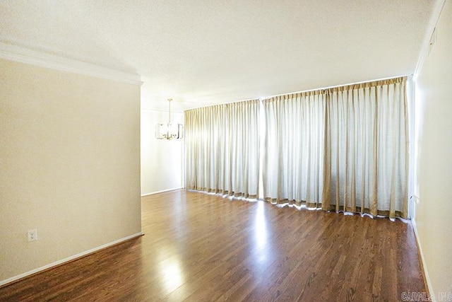 spare room featuring crown molding, baseboards, an inviting chandelier, wood finished floors, and a textured ceiling