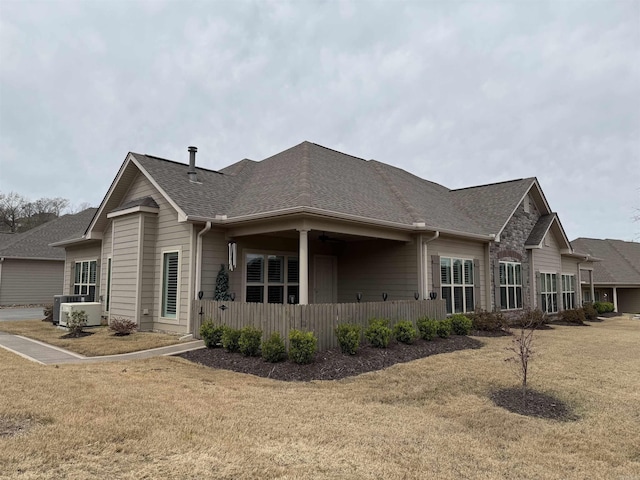 view of side of property featuring central air condition unit, a yard, and a shingled roof