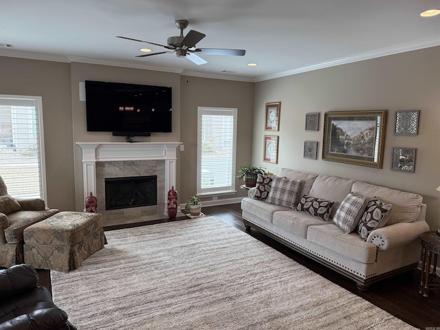 living room featuring dark wood finished floors, recessed lighting, ceiling fan, a tiled fireplace, and crown molding