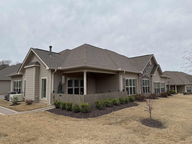 view of front of house featuring a front lawn, central air condition unit, and a shingled roof