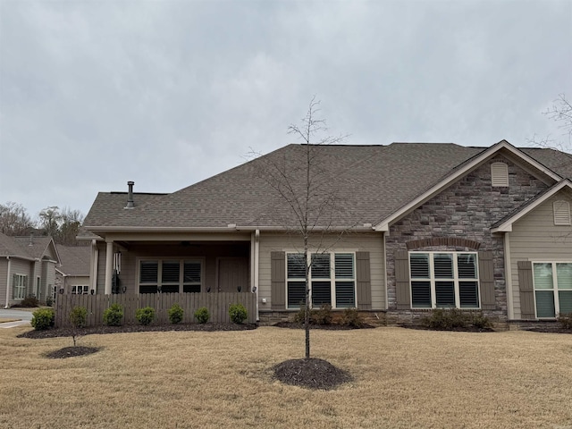 rear view of house with stone siding, a lawn, and roof with shingles