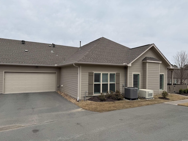view of property exterior featuring driveway, an attached garage, central AC, and a shingled roof