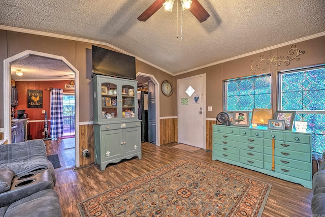 interior space with wood finished floors, lofted ceiling, ceiling fan, ornamental molding, and wainscoting