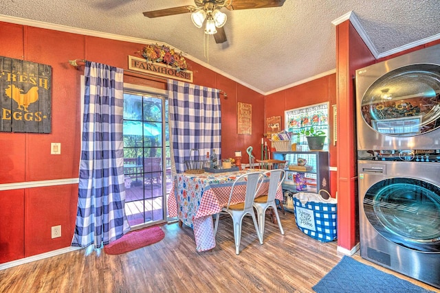 dining room featuring a ceiling fan, wood finished floors, lofted ceiling, ornamental molding, and stacked washer and dryer
