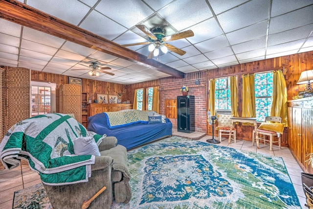 tiled living area with wooden walls, a ceiling fan, and a drop ceiling