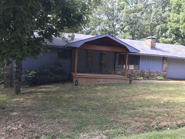 view of front of house with a front lawn, stone siding, covered porch, an attached garage, and a chimney