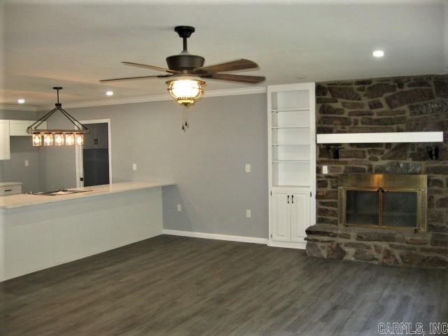 unfurnished living room with a stone fireplace, baseboards, dark wood-style flooring, and ornamental molding