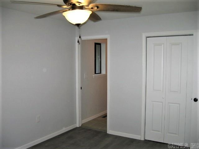 unfurnished bedroom with dark wood-style flooring, baseboards, a closet, and ceiling fan