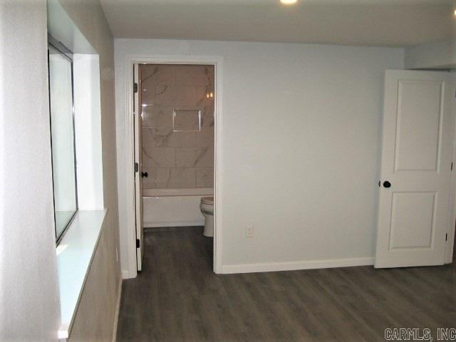 unfurnished bedroom with dark wood-style floors, baseboards, and connected bathroom