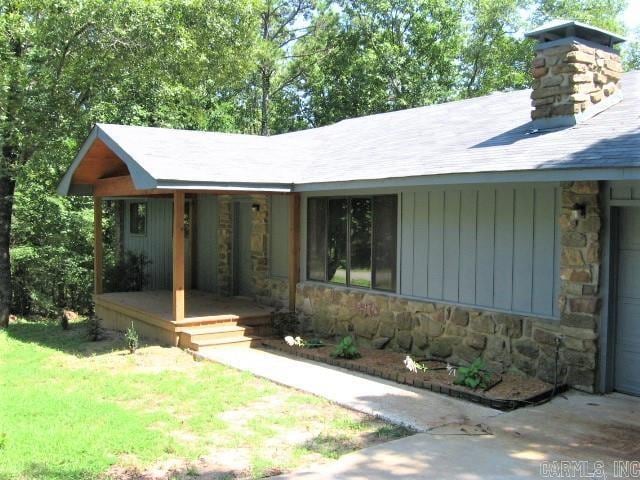 view of front of property featuring a porch, stone siding, a front yard, and a chimney