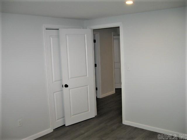 unfurnished bedroom with a closet, dark wood-type flooring, and baseboards