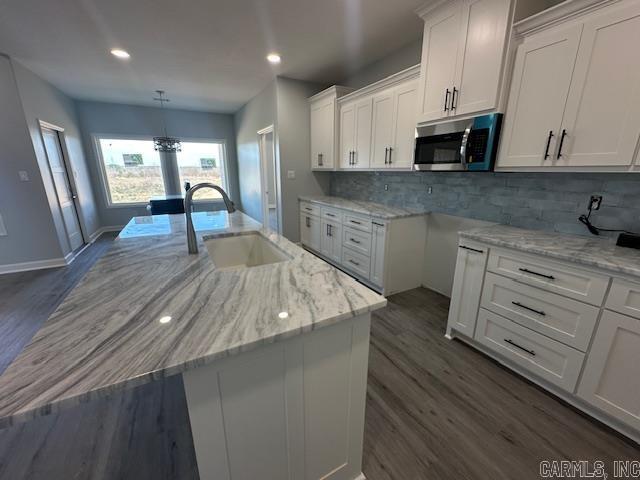kitchen featuring stainless steel microwave, white cabinets, light stone counters, and a sink