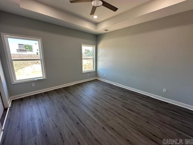 empty room with baseboards, a tray ceiling, and dark wood-style flooring