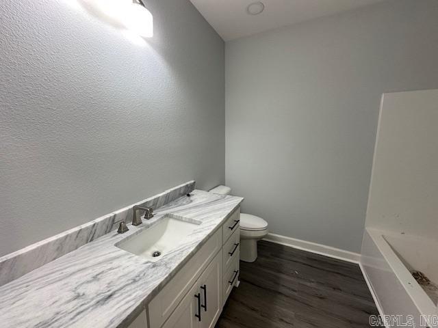 bathroom with baseboards, toilet, a bathing tub, wood finished floors, and vanity