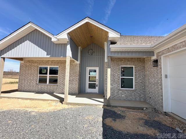 property entrance featuring brick siding, an attached garage, board and batten siding, and a patio