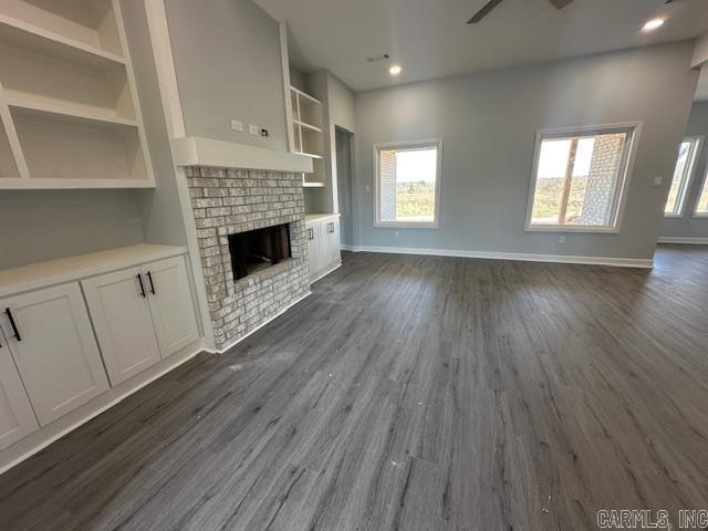 unfurnished living room featuring dark wood-style floors, built in shelves, a fireplace, and baseboards