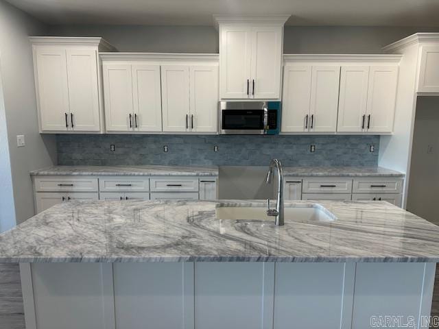 kitchen featuring a sink, stainless steel microwave, and white cabinetry