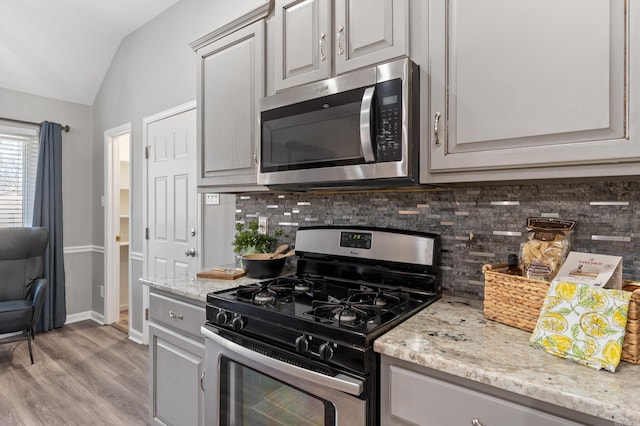 kitchen featuring light stone countertops, lofted ceiling, stainless steel appliances, light wood-style floors, and tasteful backsplash