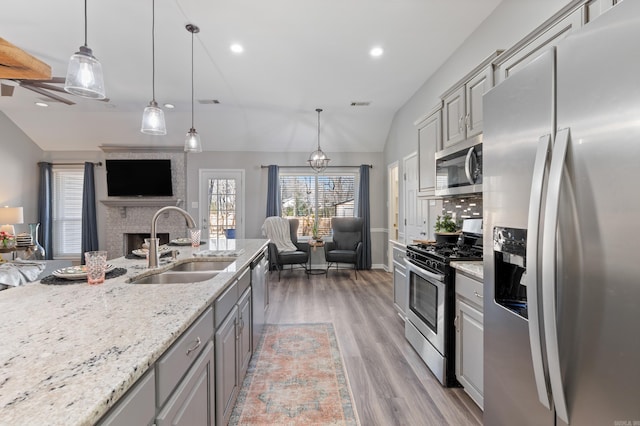 kitchen with lofted ceiling, gray cabinets, a sink, appliances with stainless steel finishes, and open floor plan