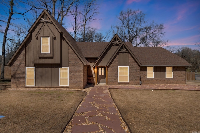 view of front of house with brick siding, a yard, board and batten siding, and roof with shingles
