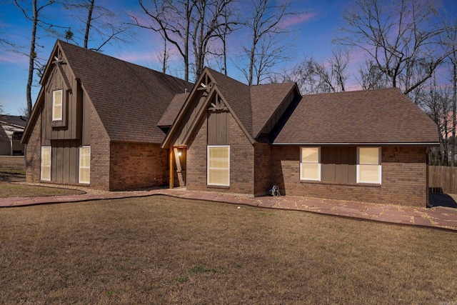 view of front facade with brick siding, a yard, and roof with shingles