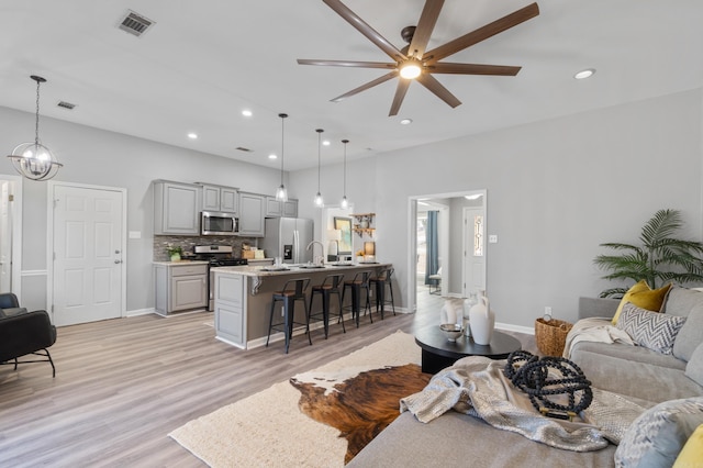 living room featuring visible vents, recessed lighting, ceiling fan with notable chandelier, and light wood-style floors
