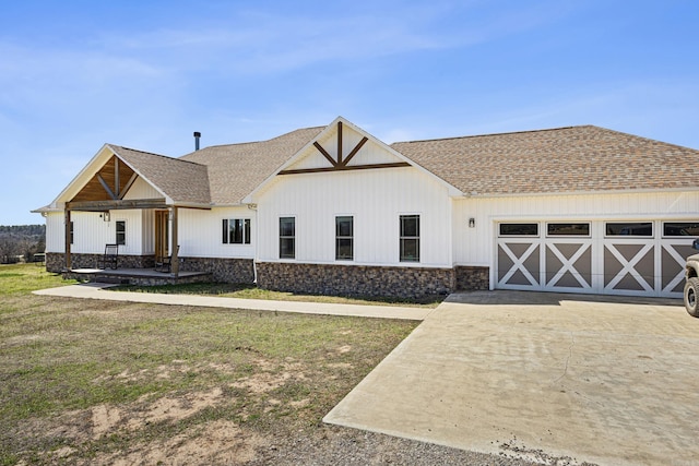 view of front facade featuring a front lawn, roof with shingles, a garage, stone siding, and driveway