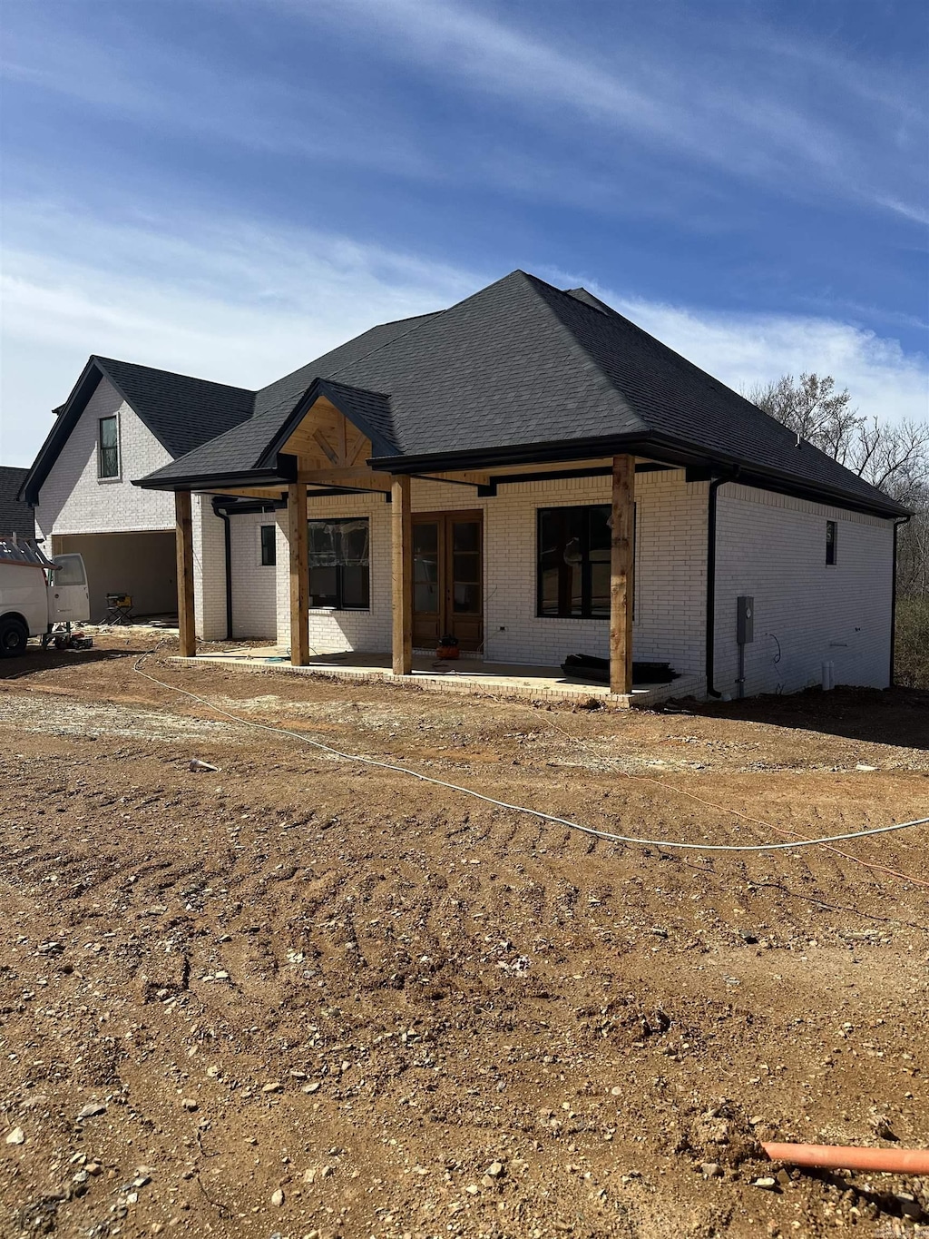view of front of home featuring brick siding, a shingled roof, and a patio