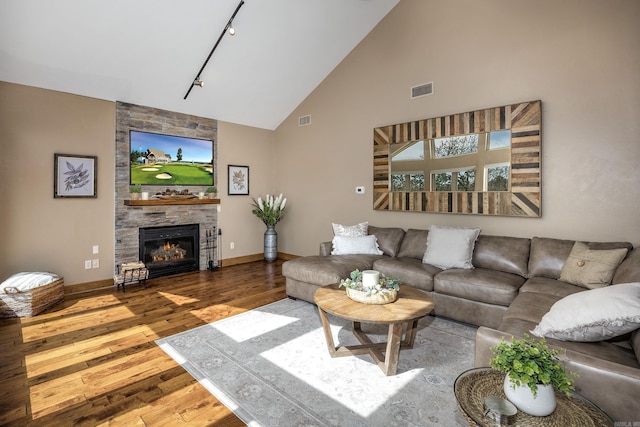 living room featuring high vaulted ceiling, a fireplace, rail lighting, baseboards, and hardwood / wood-style flooring