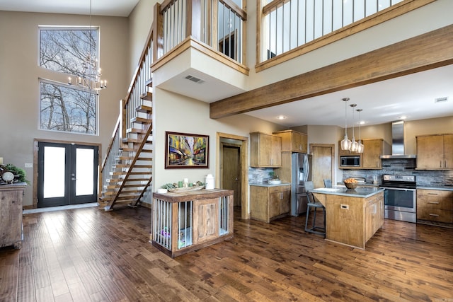 kitchen with a high ceiling, wall chimney exhaust hood, a chandelier, stainless steel appliances, and french doors