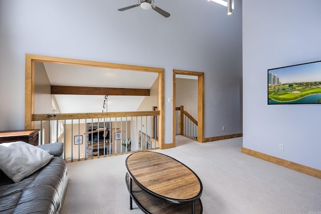 carpeted living room featuring beamed ceiling, ceiling fan, a high ceiling, and baseboards